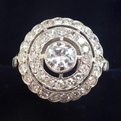 fig 1. An Art Deco platinum ring featuring a central round diamond encircled by concentric rings of smaller round diamonds with millegrain edges.