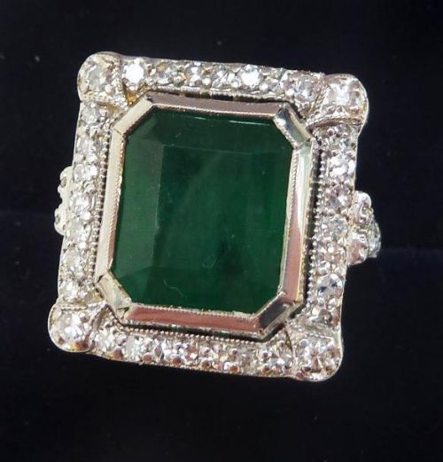 fig 1. An 18ct white gold ring featuring a large octagonal green emerald centrepiece framed by a border of small round diamonds.