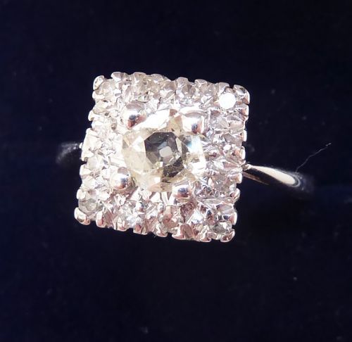 fig 1. An Art Deco 18ct white gold ring featuring a central round diamond surrounded by a square cluster of smaller diamonds.