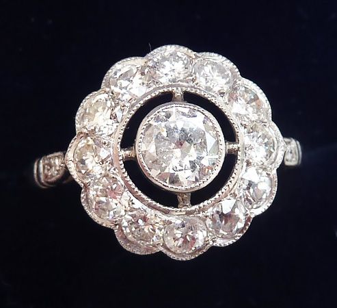 fig 1. An Art Deco platinum ring featuring a central round diamond encircled by a scalloped daisy cluster setting of diamonds with millegrain edges.