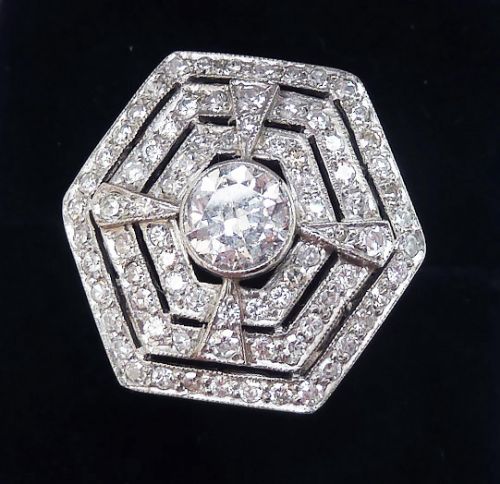 fig 1. An Art Deco hexagonal target ring crafted in platinum, featuring a central bezel-set round diamond surrounded by geometric concentric bands of smaller diamonds with millegrain borders.