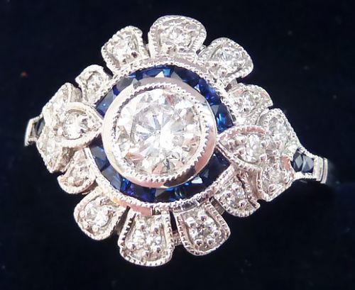 fig 2. An Art Deco white gold target ring featuring a central round diamond encircled by calibre-cut blue sapphires and a outer scalloped diamond halo with milgrain borders.