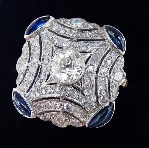 fig 1. An Art Deco platinum and diamond cluster ring featuring a central round diamond surrounded by smaller pave diamonds and four blue sapphires at the corners.