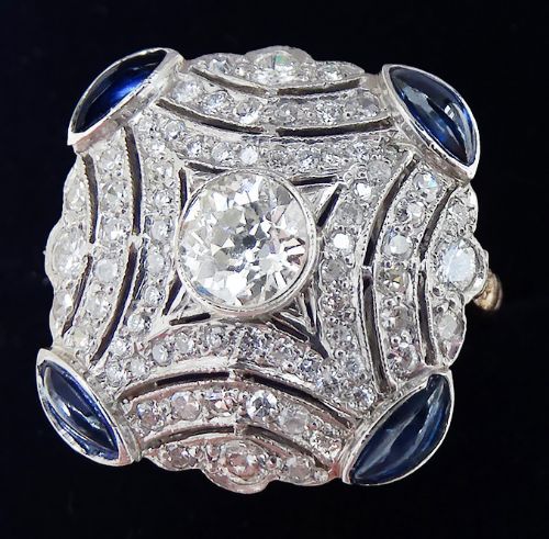 fig 2. An Art Deco platinum and diamond cluster ring featuring a central round diamond surrounded by smaller pave diamonds and four blue sapphires at the corners.