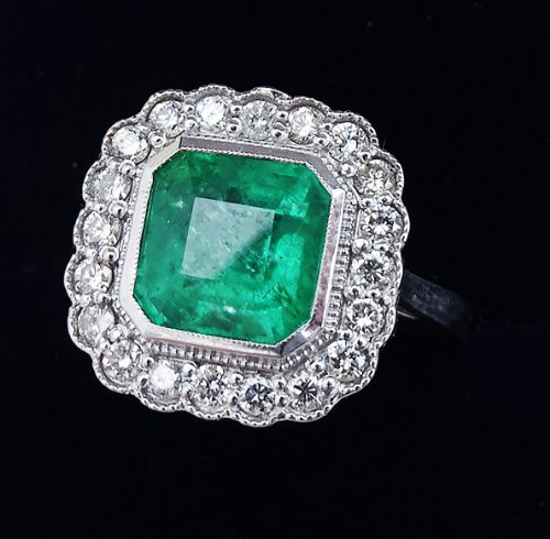 fig 1. An Art Deco style white gold ring featuring a central octagonal emerald-cut green emerald surrounded by a halo of brilliant-cut diamonds with milgrain edging.