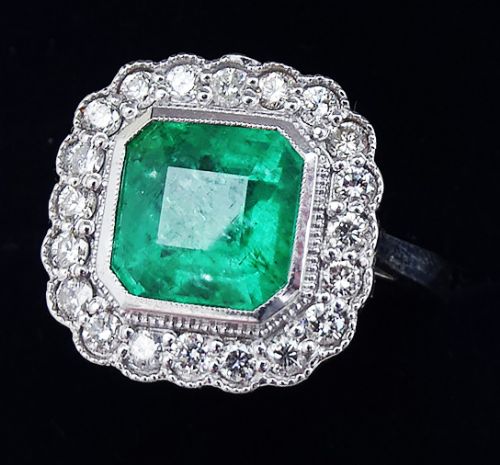fig 2. An Art Deco style white gold ring featuring a central octagonal emerald-cut green emerald surrounded by a halo of brilliant-cut diamonds with milgrain edging.