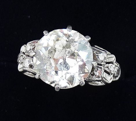 fig 1. An Art Deco 18ct white gold ring featuring a central round diamond solitaire flanked by carved, diamond-set shoulders.