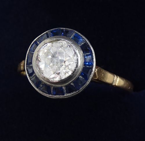 fig 1. An Art Deco target ring featuring a central round diamond surrounded by a halo of calibre-cut blue sapphires on a gold band.