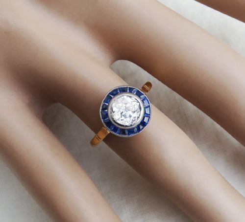 fig 2. An Art Deco target ring featuring a central round diamond surrounded by a halo of calibre-cut blue sapphires on a gold band.