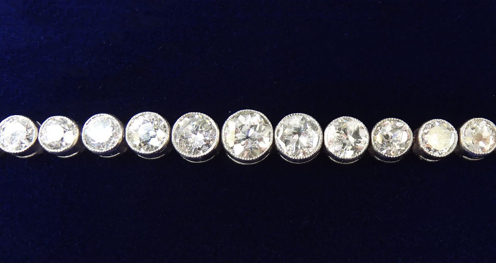 An Art Deco platinum line bracelet set with a row of graduated round diamonds in rub-over bezel settings.