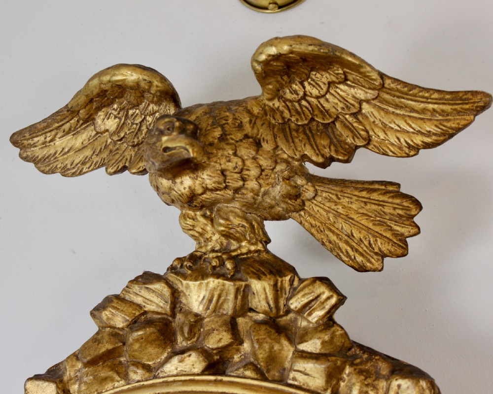 A circular giltwood convex mirror topped with a carved eagle finial and decorated with ball ornaments around the frame and foliage at the base. View II
