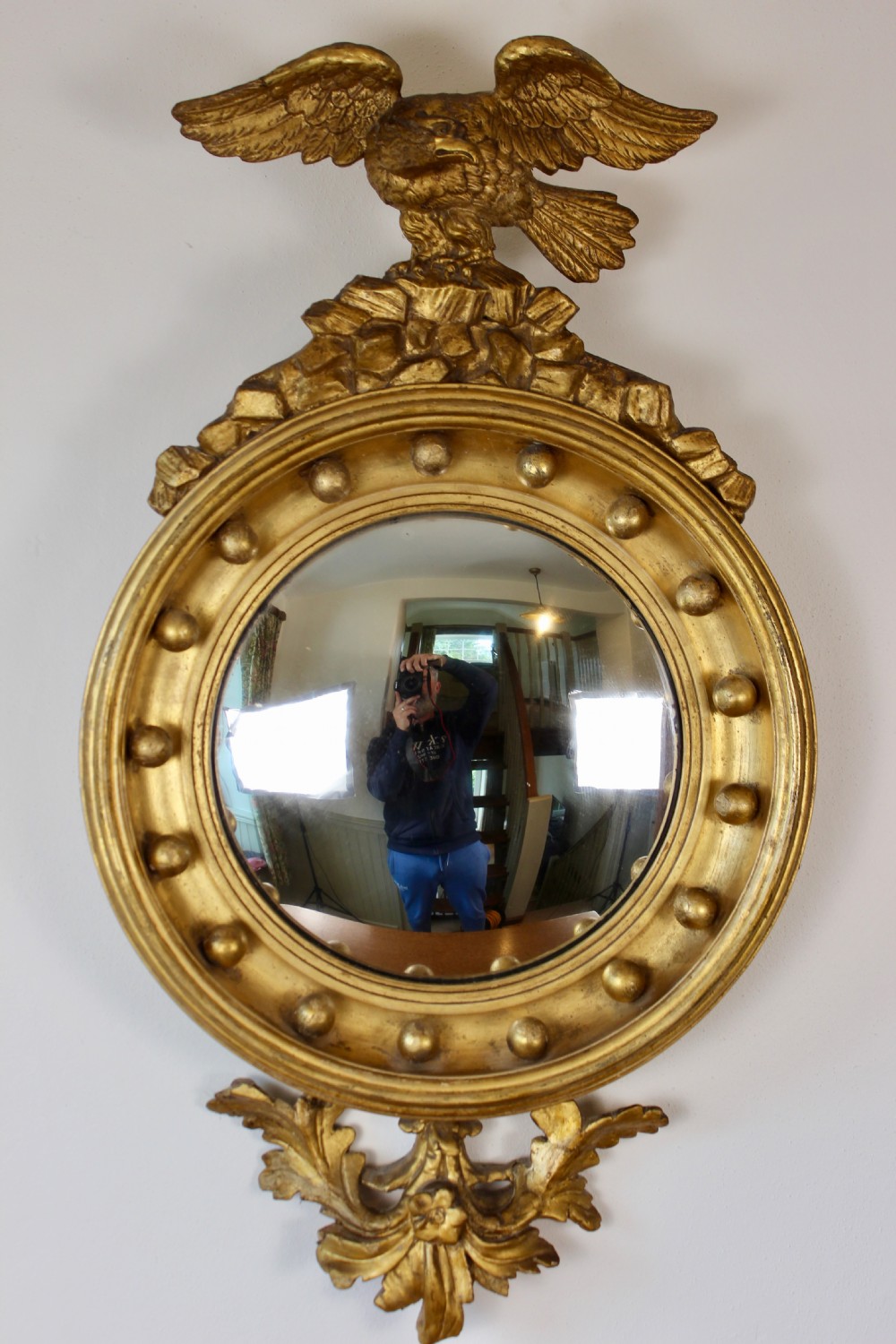 A circular giltwood convex mirror topped with a carved eagle finial and decorated with ball ornaments around the frame and foliage at the base.