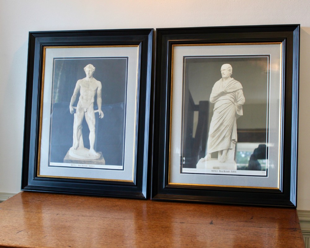 A pair of black and white framed photographic prints depicting ancient classical statues from the Naples National Archaeological Museum in dark stepped frames with gold accents.