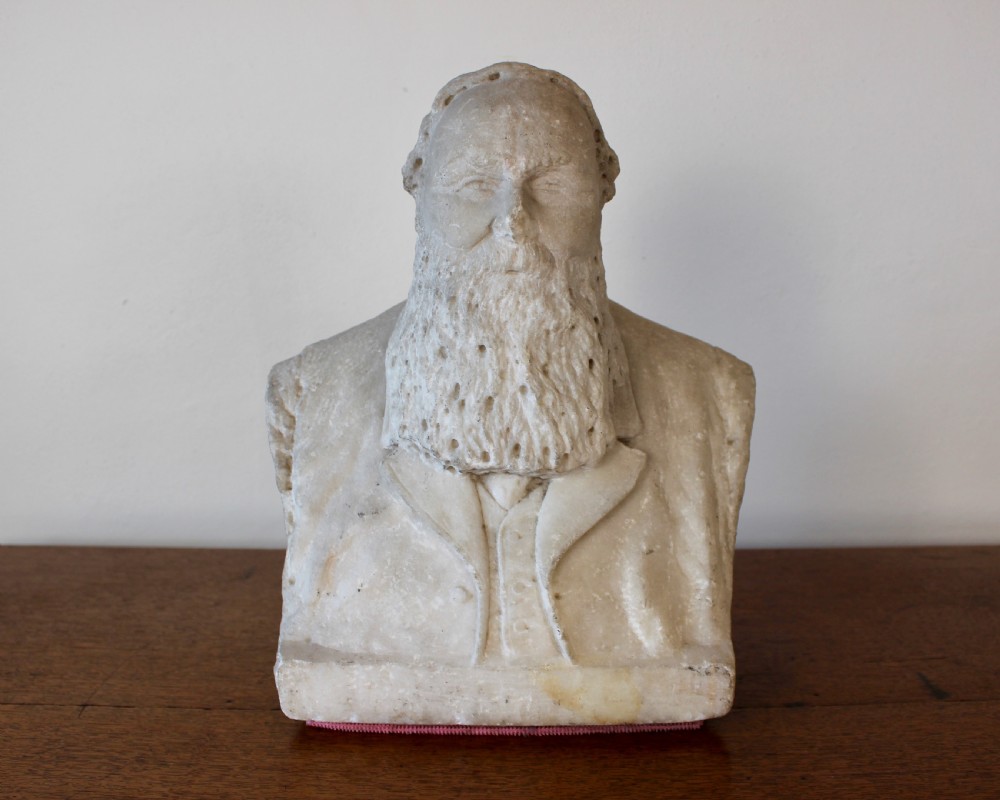 A carved off-white marble bust representing a bearded man wearing a Victorian jacket and waistcoat, set on an integrated square plinth base. View III