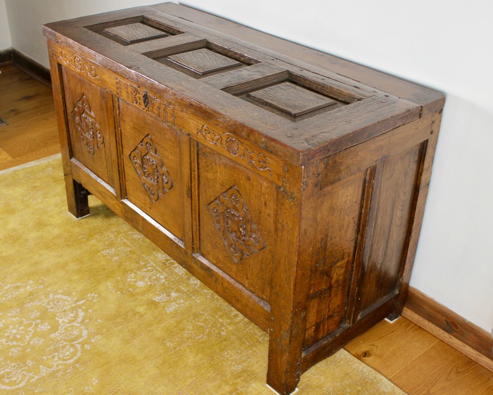 A dark oak coffer featuring three carved front panels with geometric lozenge motifs and a panelled hinged lid.