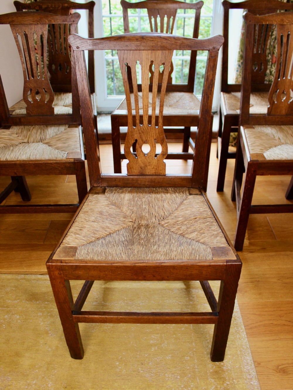 A set of eight George III oak country dining chairs with pierced splat backs and woven rush seats. View II