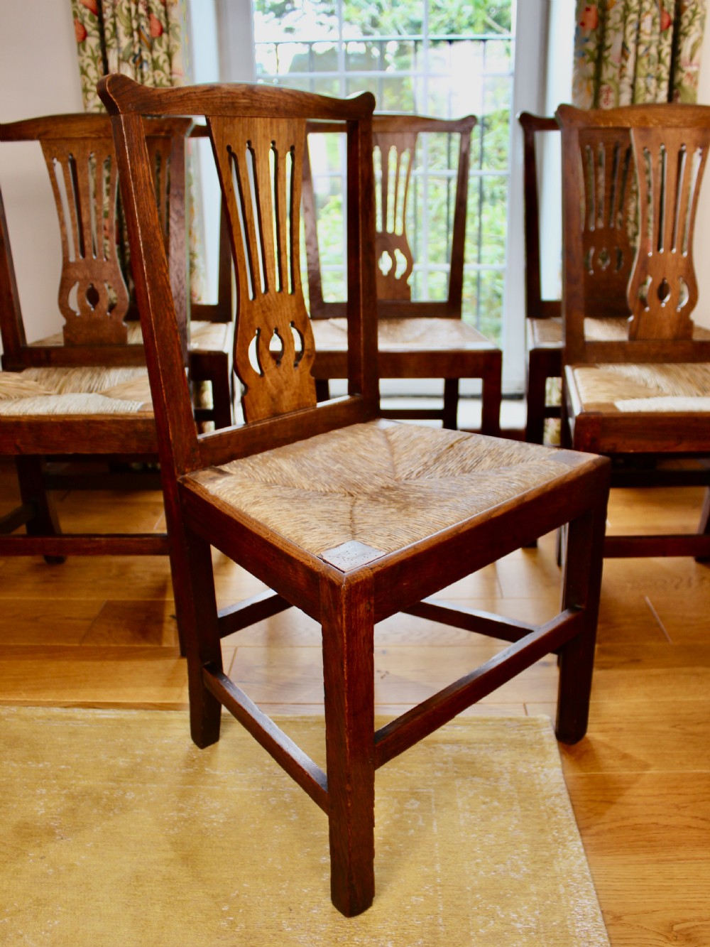 A set of eight George III oak country dining chairs with pierced splat backs and woven rush seats. View III