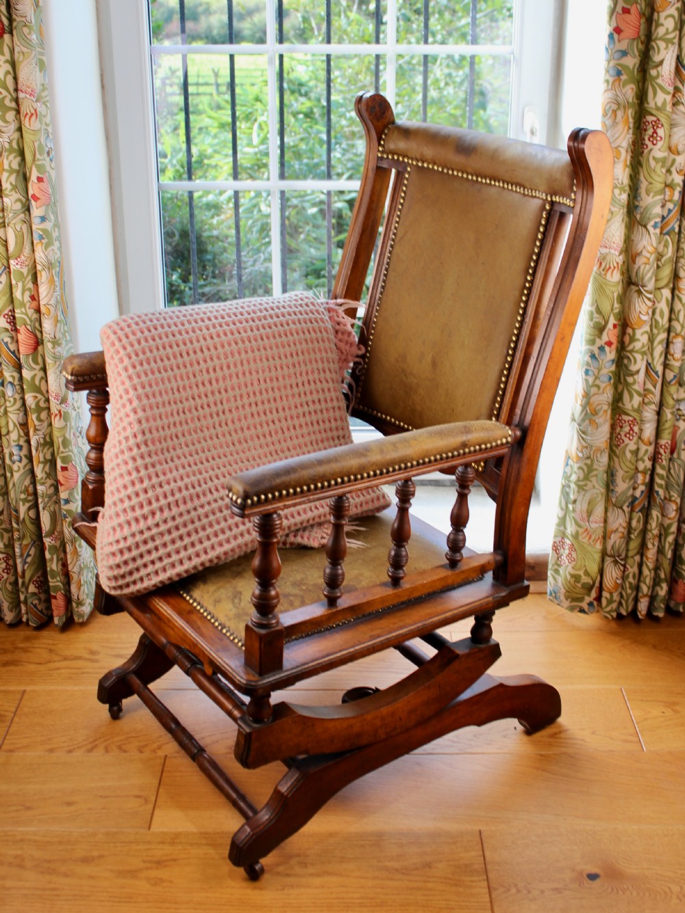 An Edwardian mahogany platform rocking chair with patinated leather upholstery, brass stud detail, and turned spindles.