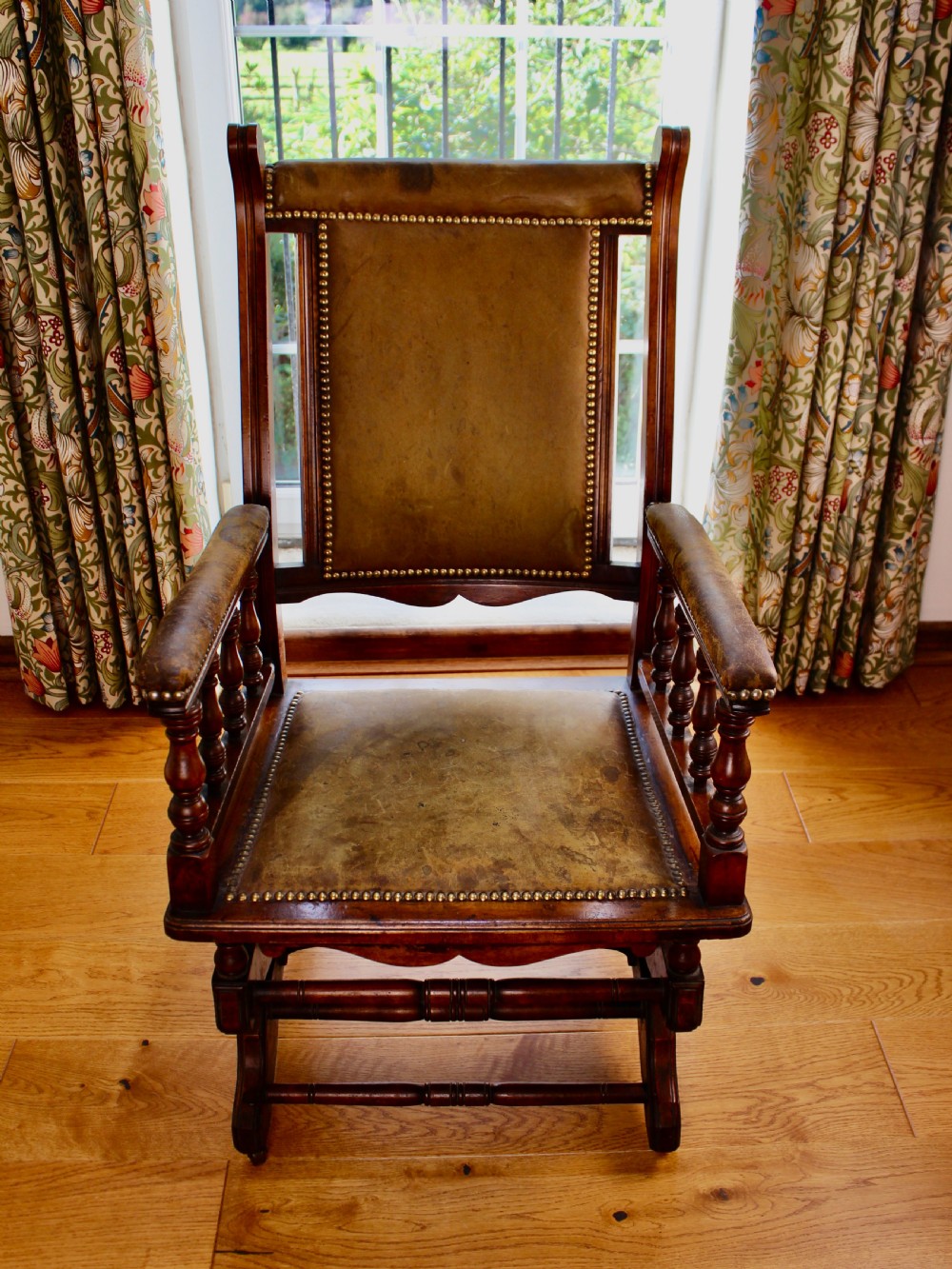 An Edwardian mahogany platform rocking chair with patinated leather upholstery, brass stud detail, and turned spindles. View II