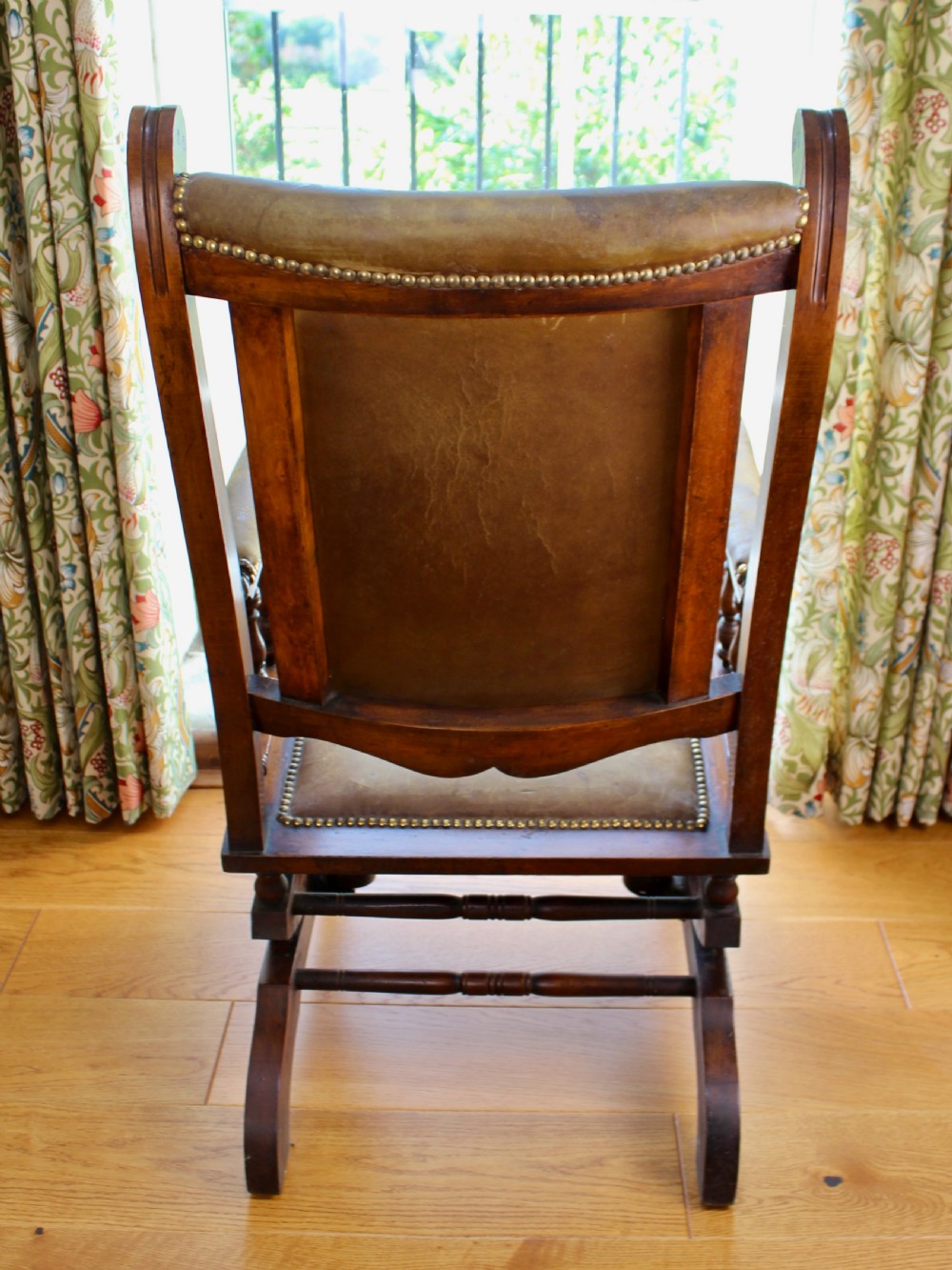 An Edwardian mahogany platform rocking chair with patinated leather upholstery, brass stud detail, and turned spindles. View III