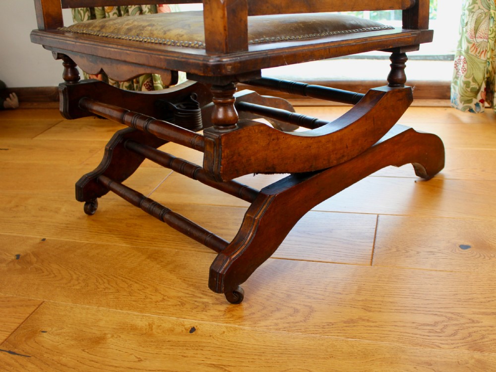An Edwardian mahogany platform rocking chair with patinated leather upholstery, brass stud detail, and turned spindles. View V