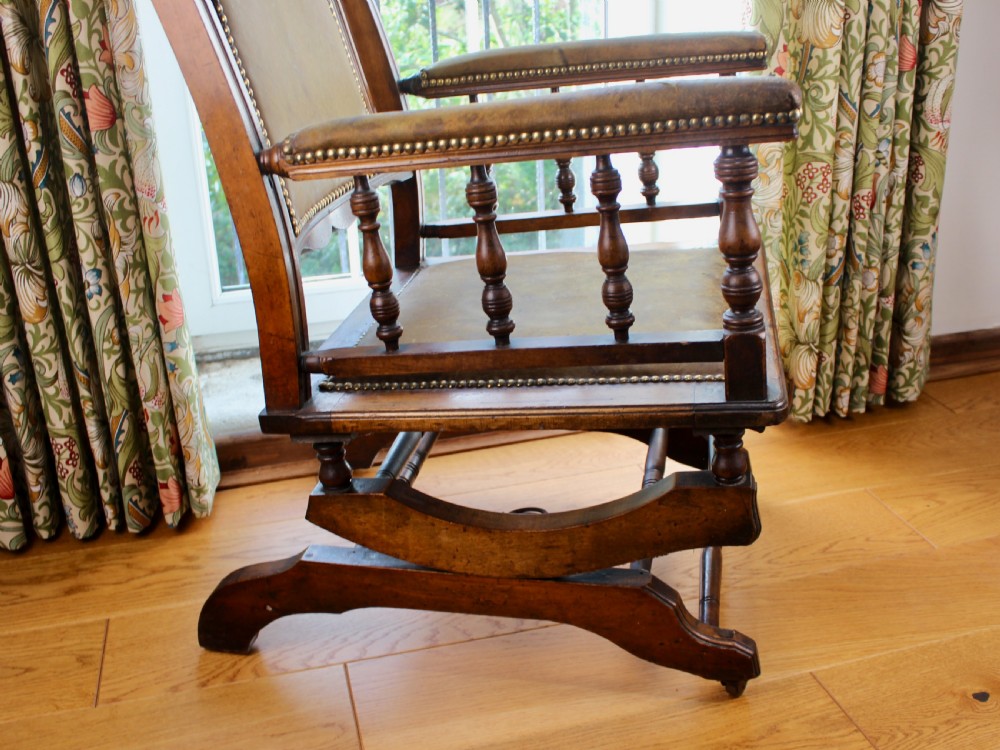An Edwardian mahogany platform rocking chair with patinated leather upholstery, brass stud detail, and turned spindles. View VI