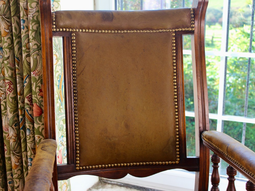 An Edwardian mahogany platform rocking chair with patinated leather upholstery, brass stud detail, and turned spindles. View VII