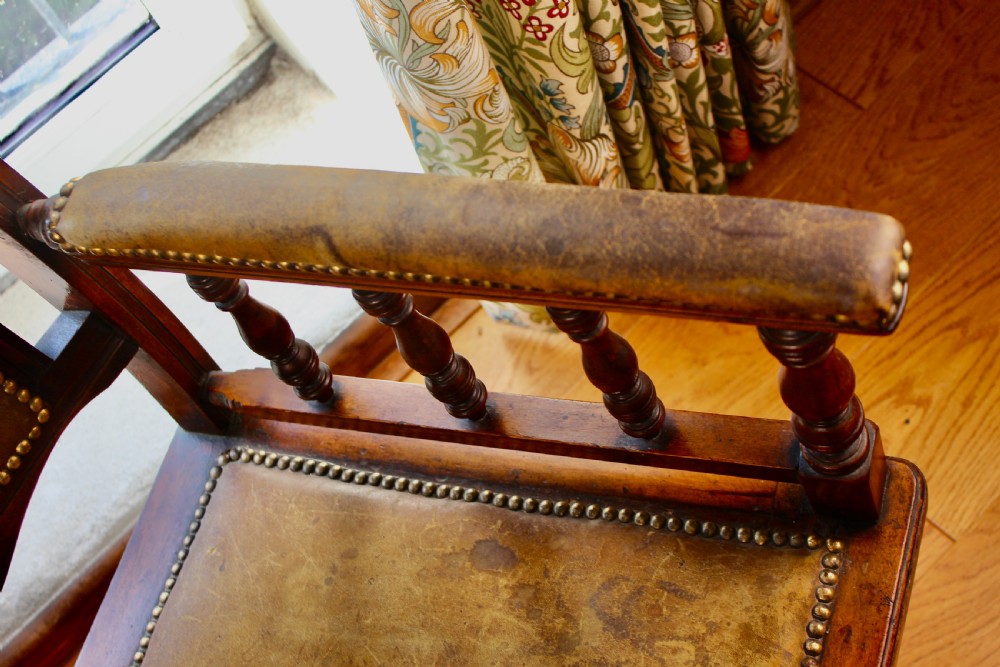 An Edwardian mahogany platform rocking chair with patinated leather upholstery, brass stud detail, and turned spindles. View X