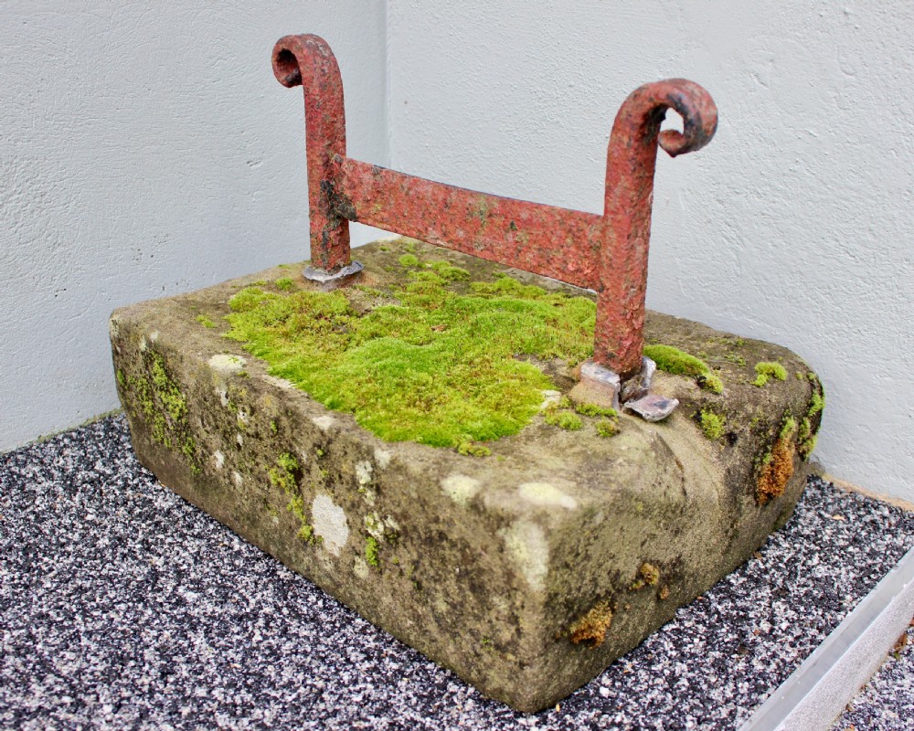 A late Georgian boot scraper featuring a wrought iron blade with scrolled side supports, anchored into a rectangular weathered stone block covered in moss. View II