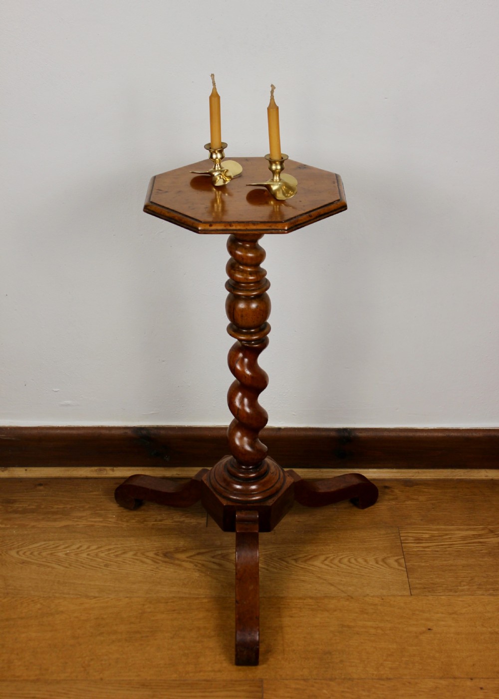 An antique William and Mary walnut candle stand featuring an octagonal top, a central barley-twist column, and a tripod base.