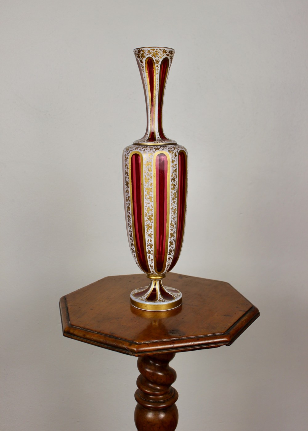 A nineteenth-century Bohemian ruby glass vase featuring white cased glass panels cut to clear with intricate gilt floral ornamentation.