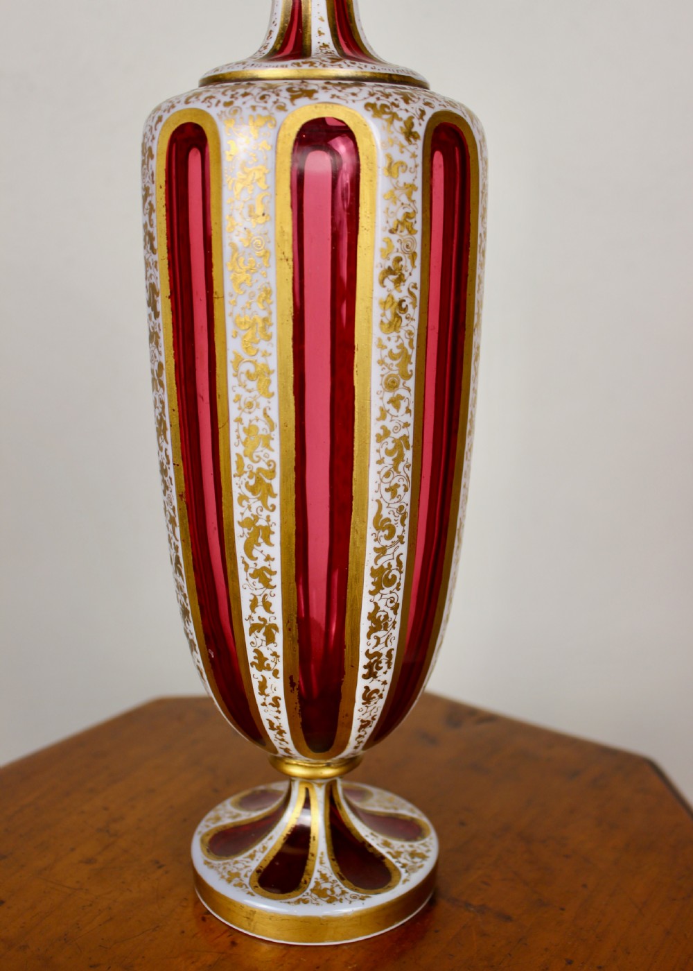 A nineteenth-century Bohemian ruby glass vase featuring white cased glass panels cut to clear with intricate gilt floral ornamentation. View III