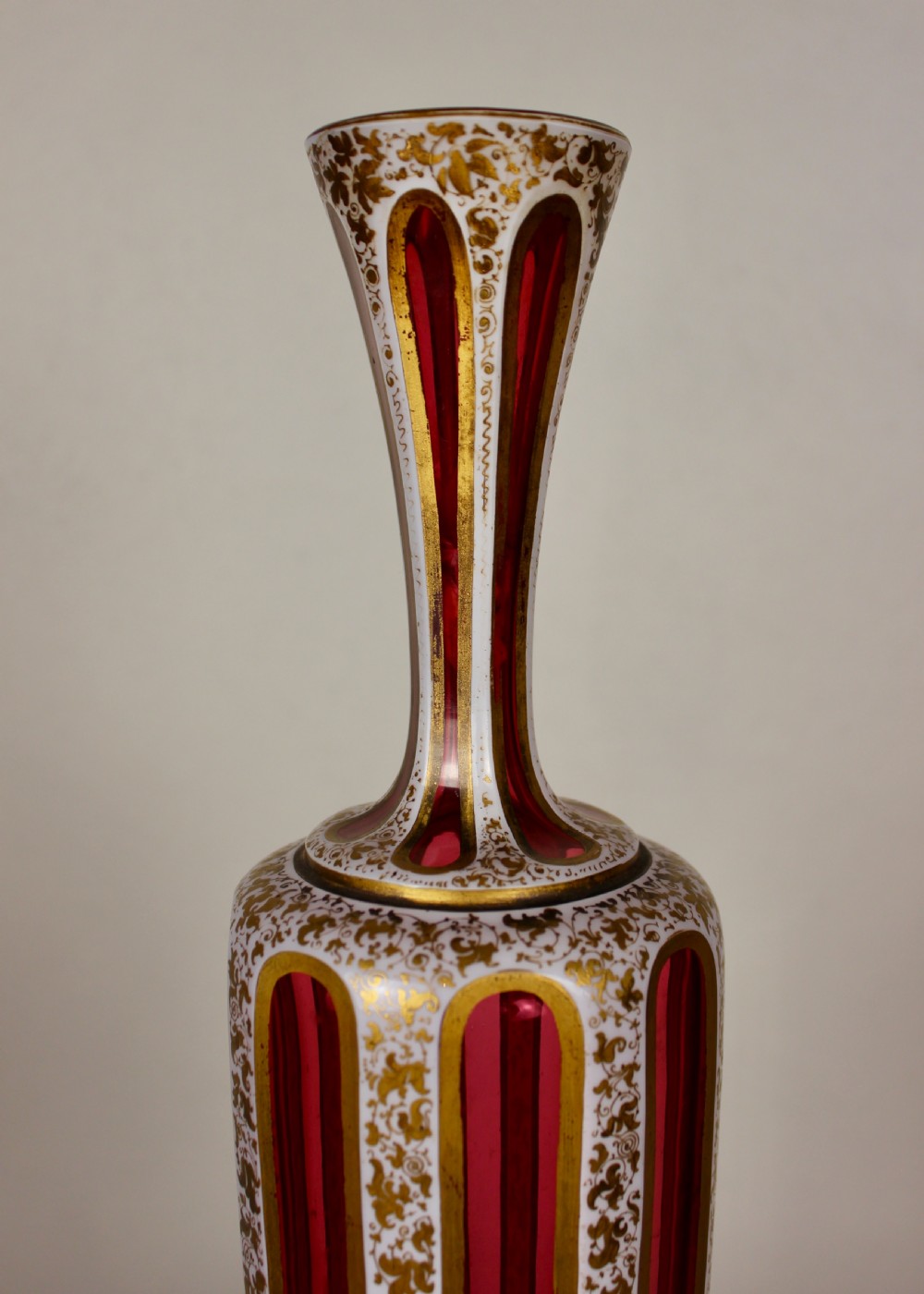 A nineteenth-century Bohemian ruby glass vase featuring white cased glass panels cut to clear with intricate gilt floral ornamentation. View IV