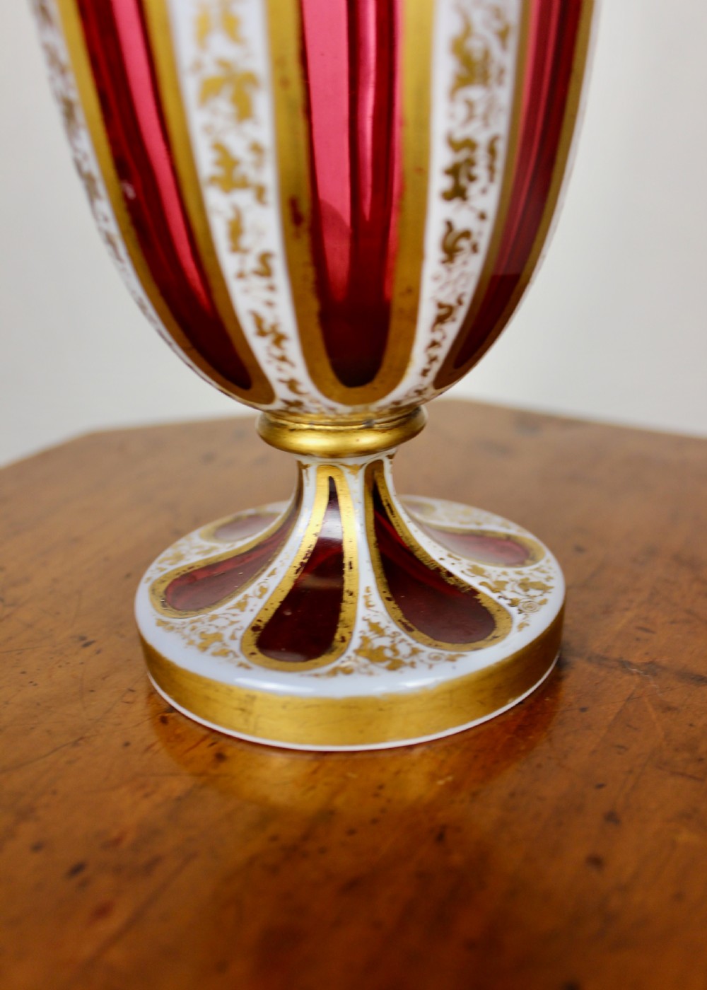 A nineteenth-century Bohemian ruby glass vase featuring white cased glass panels cut to clear with intricate gilt floral ornamentation. View V