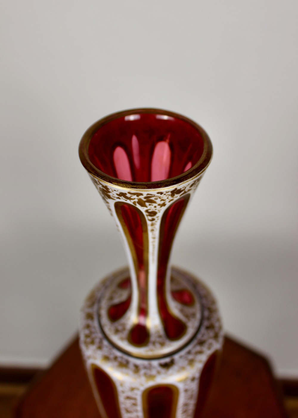 A nineteenth-century Bohemian ruby glass vase featuring white cased glass panels cut to clear with intricate gilt floral ornamentation. View VI