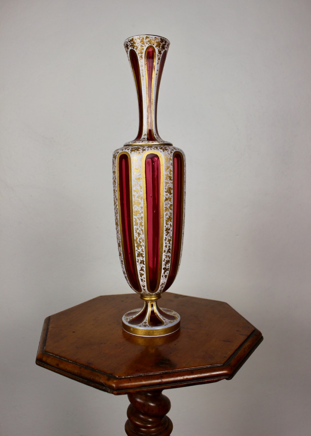 A nineteenth-century Bohemian ruby glass vase featuring white cased glass panels cut to clear with intricate gilt floral ornamentation. View VIII