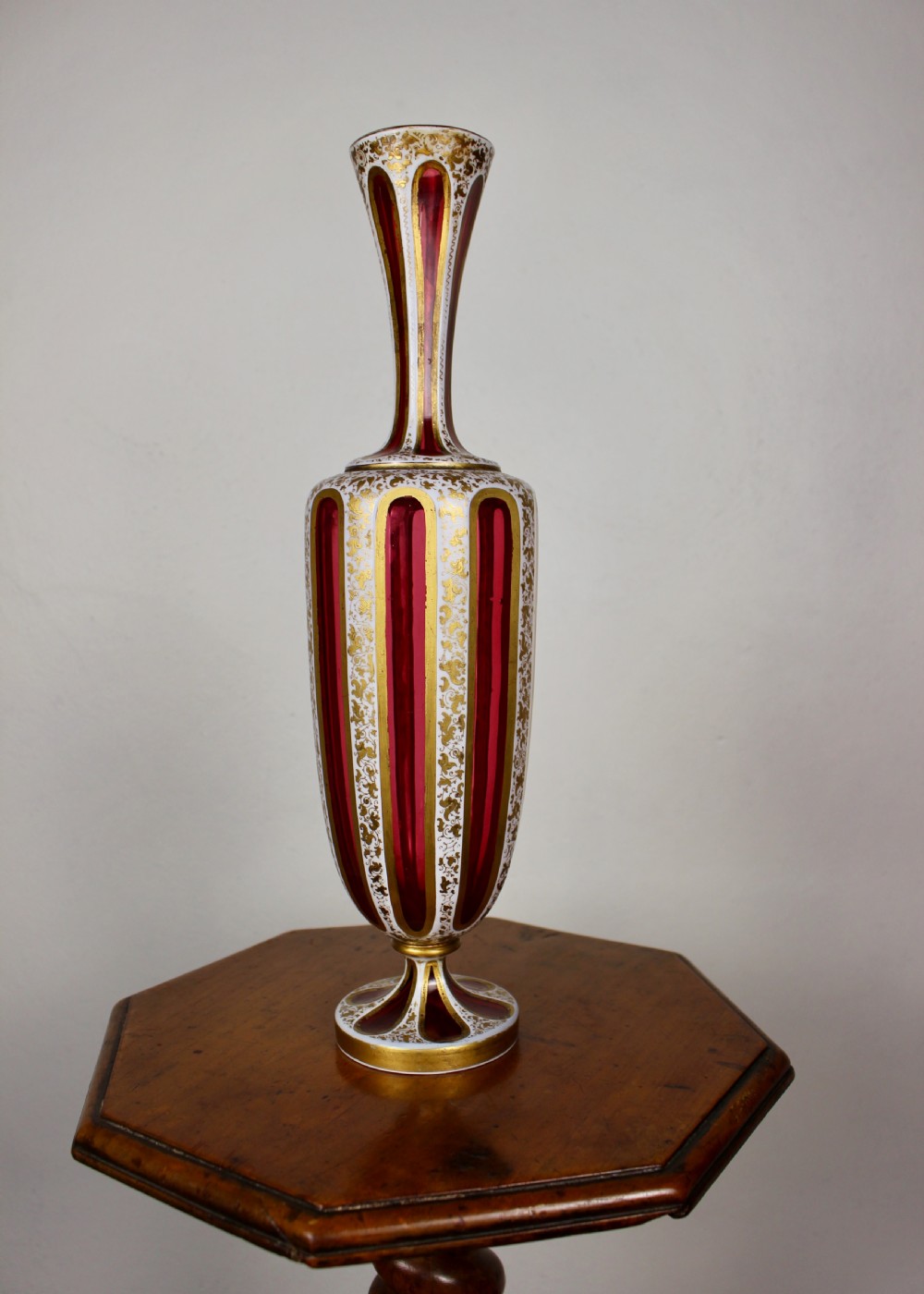 A nineteenth-century Bohemian ruby glass vase featuring white cased glass panels cut to clear with intricate gilt floral ornamentation. View IX