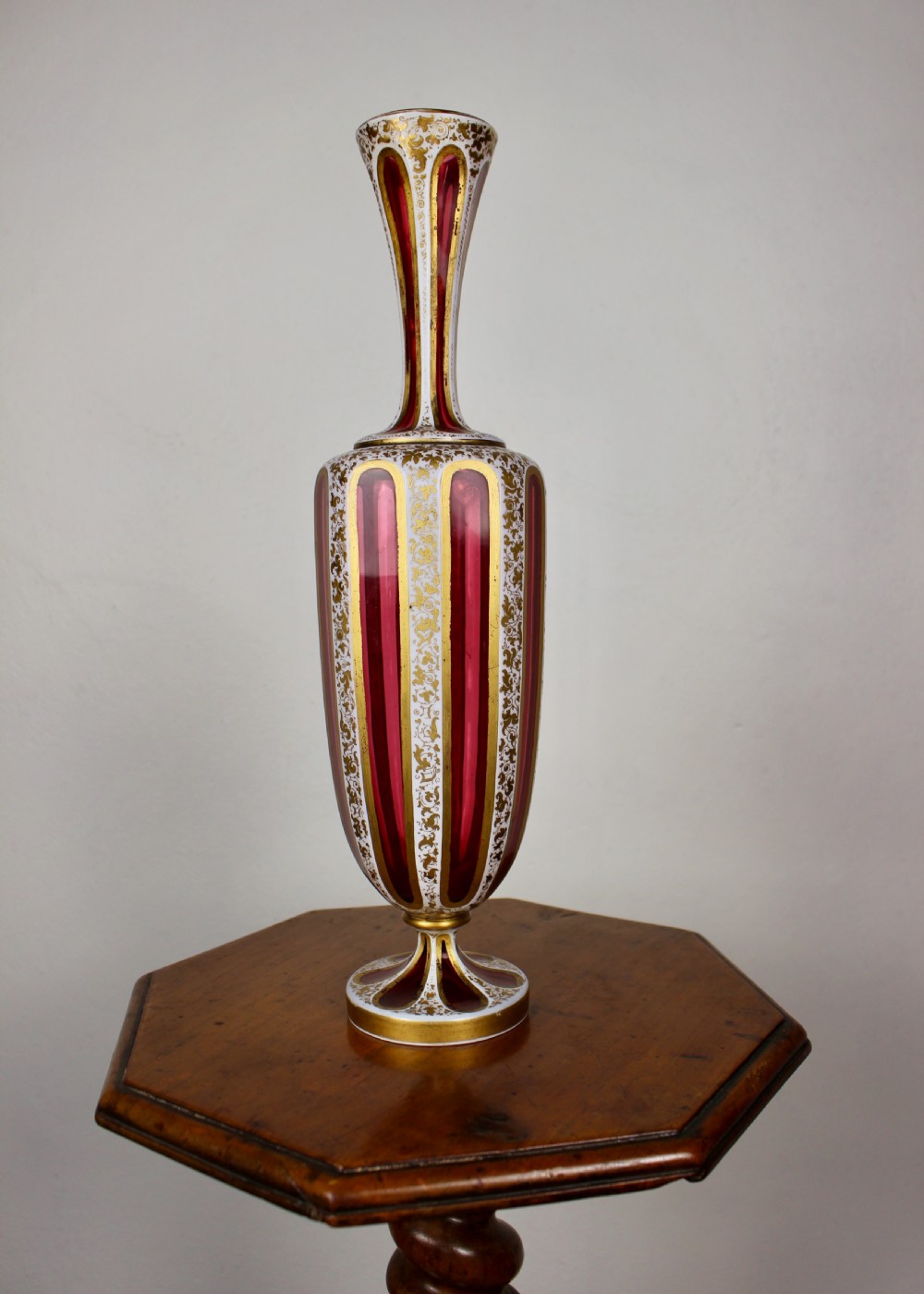 A nineteenth-century Bohemian ruby glass vase featuring white cased glass panels cut to clear with intricate gilt floral ornamentation. View X
