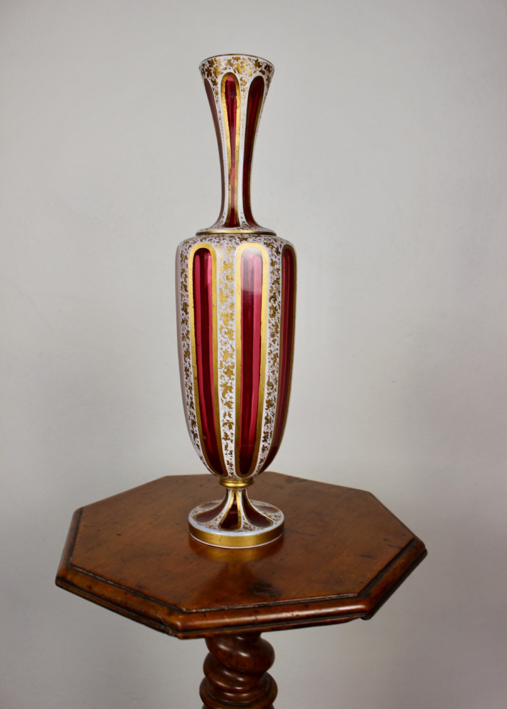 A nineteenth-century Bohemian ruby glass vase featuring white cased glass panels cut to clear with intricate gilt floral ornamentation. View XI