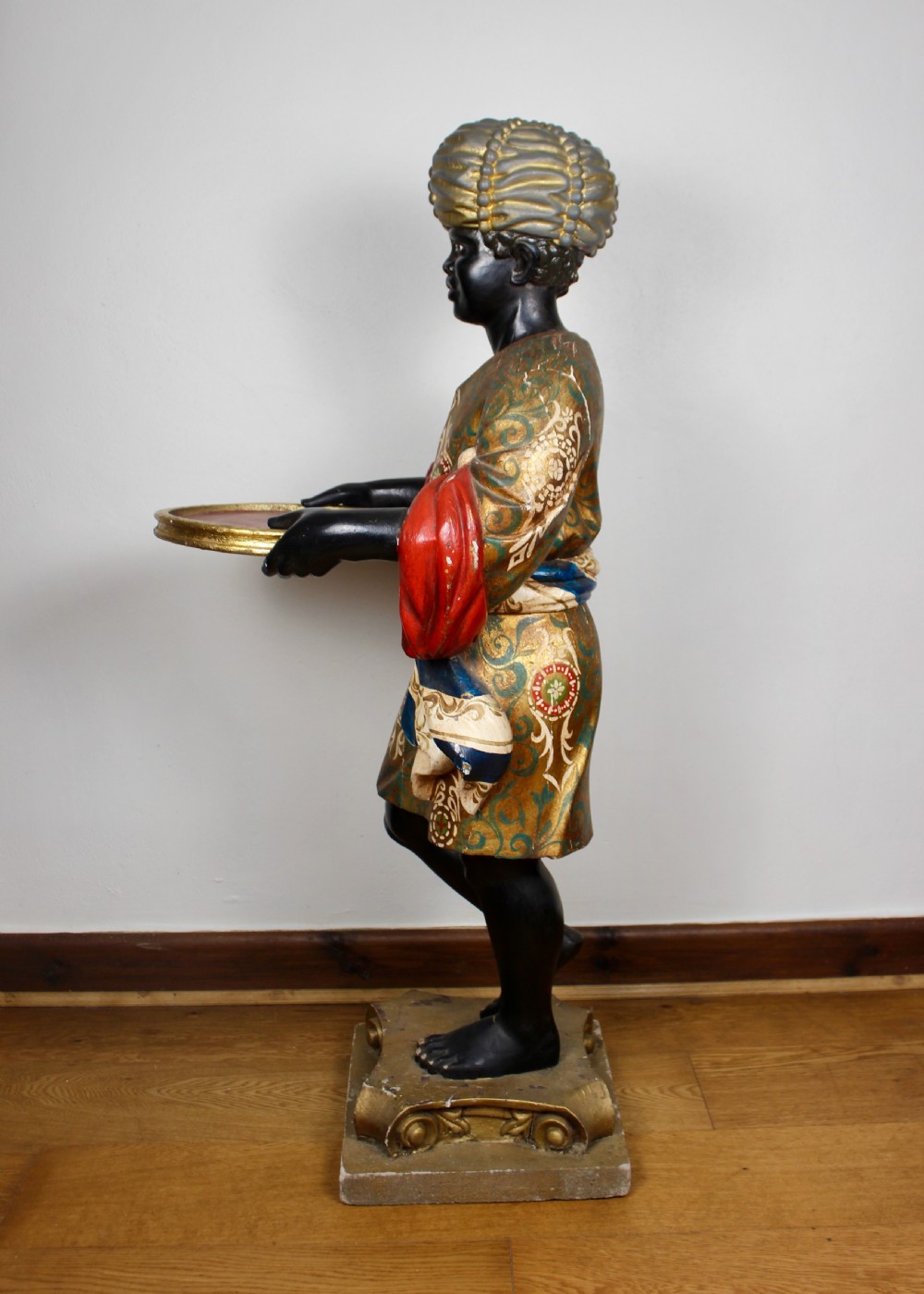 A carved wooden standing Venetian waiter figure wearing a decorated gold tunic and turban while holding a tray on a carved base. View VII