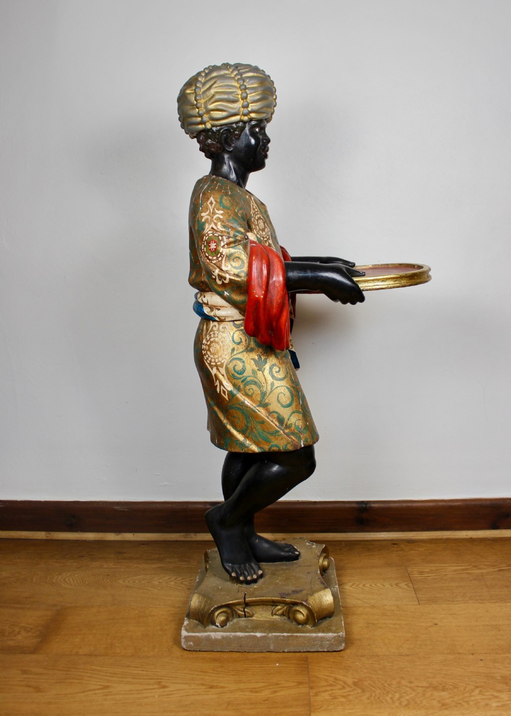 A carved wooden standing Venetian waiter figure wearing a decorated gold tunic and turban while holding a tray on a carved base. View IX