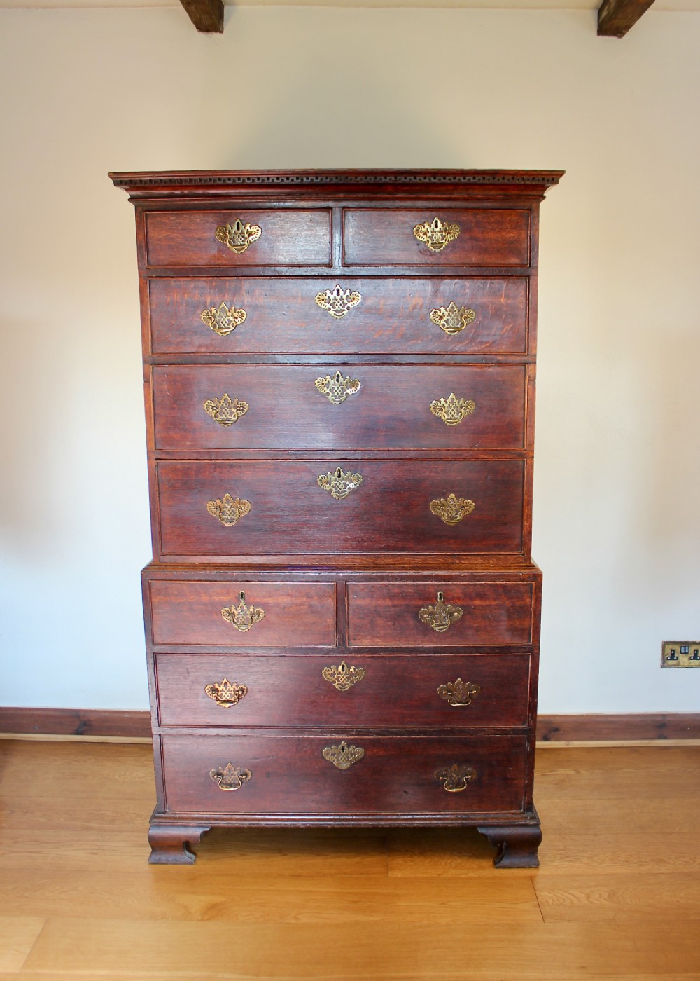 A tall George III dark oak chest-on-chest featuring two short over five long graduated drawers adorned with ornate brass handles and supported on ogee bracket feet.