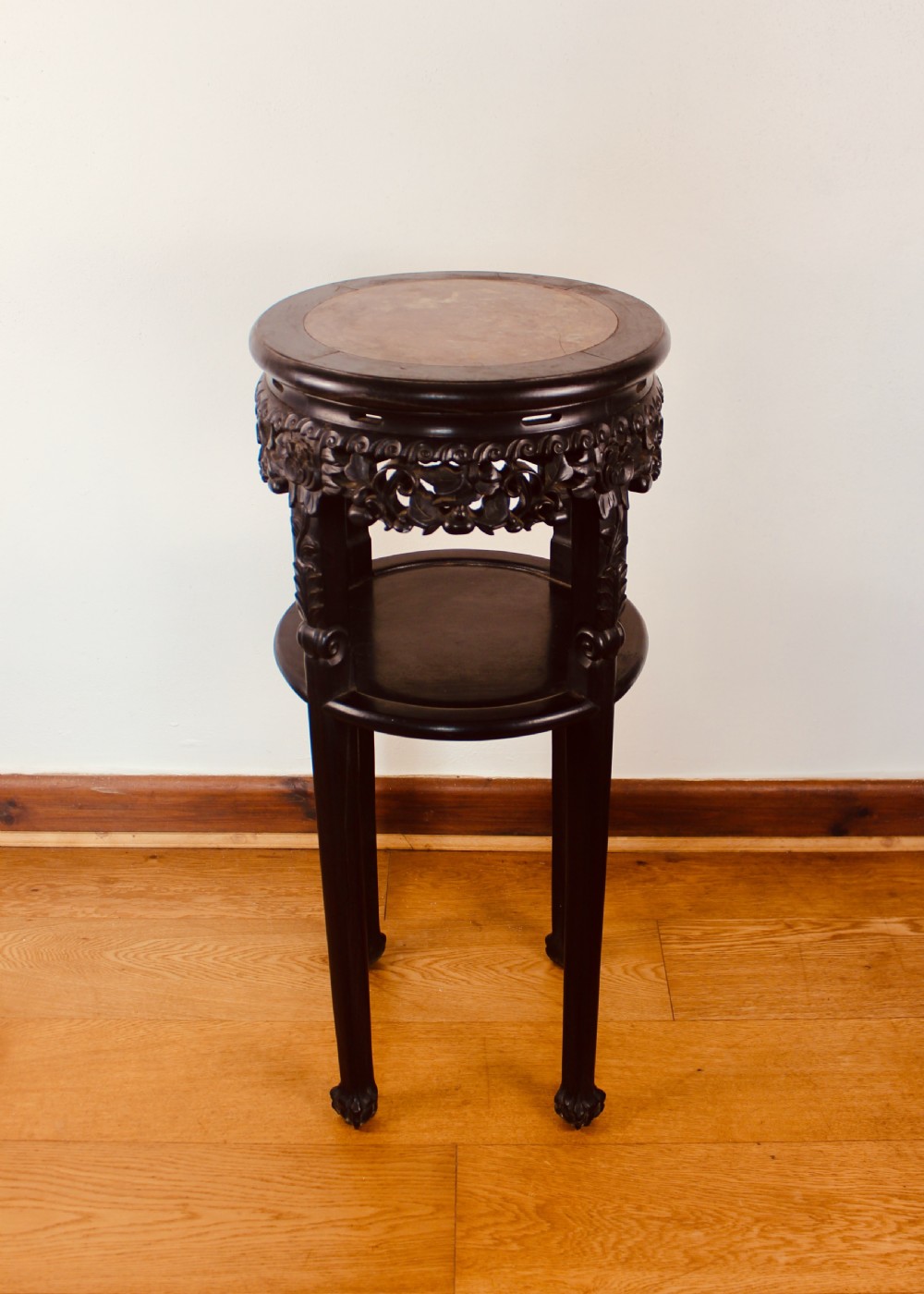 A tall dark hardwood circular jardiniere stand featuring an inset marble top, a pierced carved frieze, a lower circular undertier, and four slender legs.