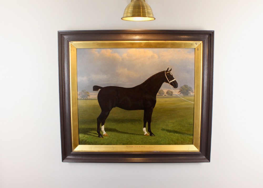 An antique framed oil painting depicting a dark brown Hackney horse standing in profile across a green pasture under a cloudy sky.