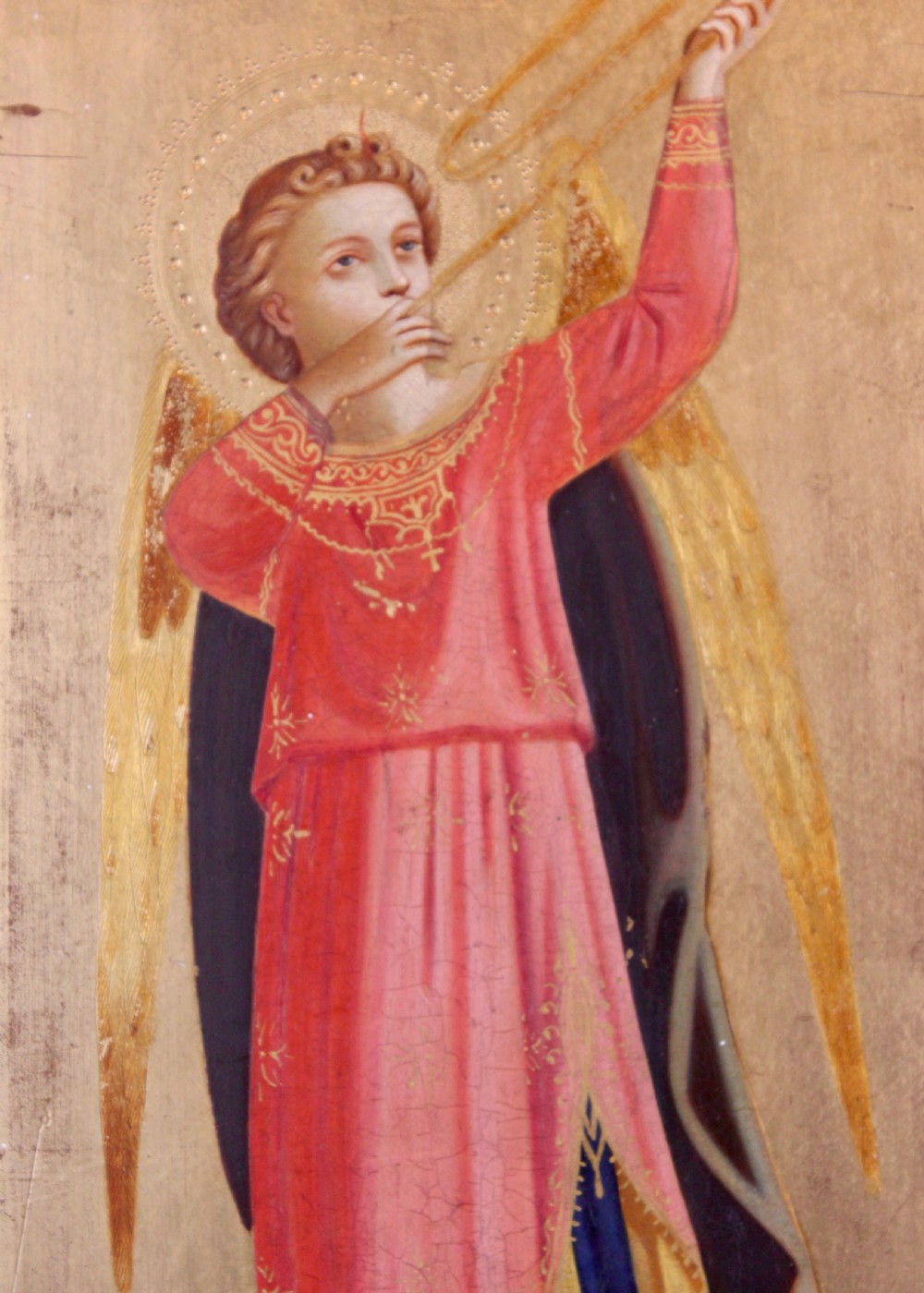 A tall arched wooden panel featuring gold leaf gilding and a central painted figure of an angel wearing a red robe and holding a long trumpet. View II