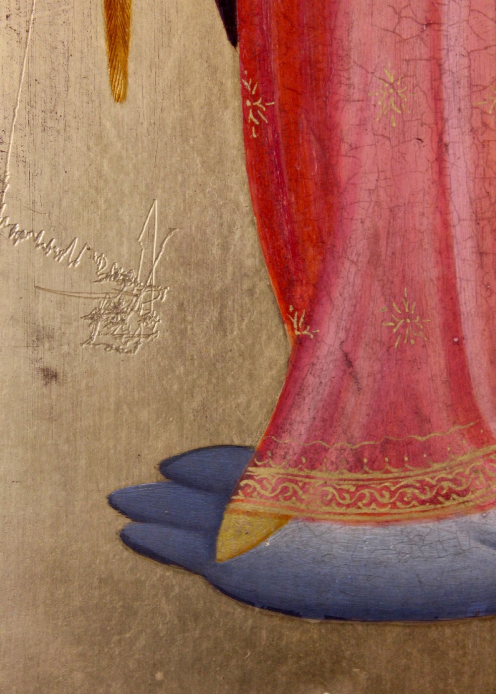 A tall arched wooden panel featuring gold leaf gilding and a central painted figure of an angel wearing a red robe and holding a long trumpet. View IV