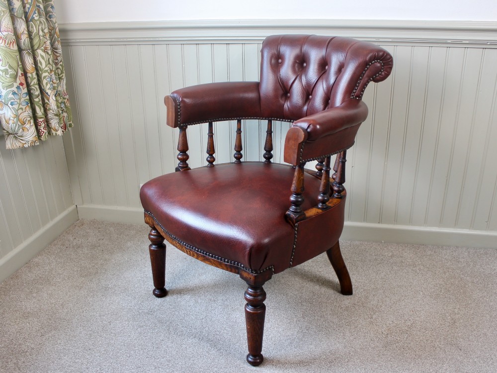 A Victorian oak elbow chair featuring deep buttoned reddish-brown leather upholstery, turned spindles, metal stud trim, and turned front legs.