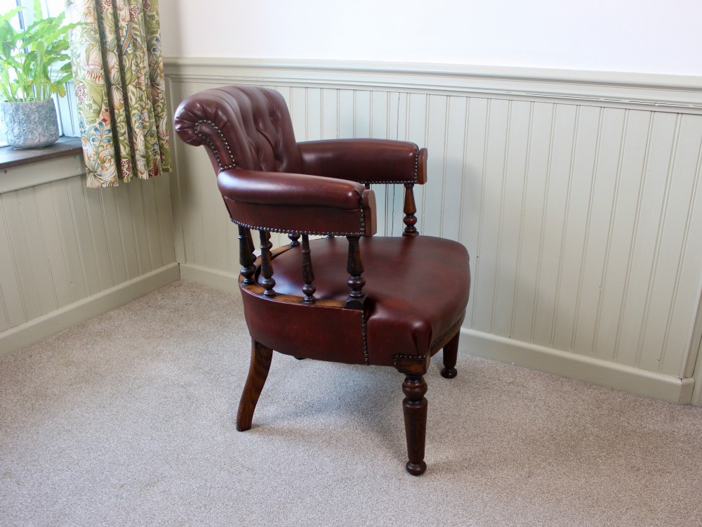 A Victorian oak elbow chair featuring deep buttoned reddish-brown leather upholstery, turned spindles, metal stud trim, and turned front legs. View IV