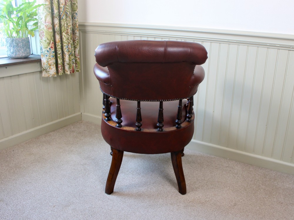 A Victorian oak elbow chair featuring deep buttoned reddish-brown leather upholstery, turned spindles, metal stud trim, and turned front legs. View V