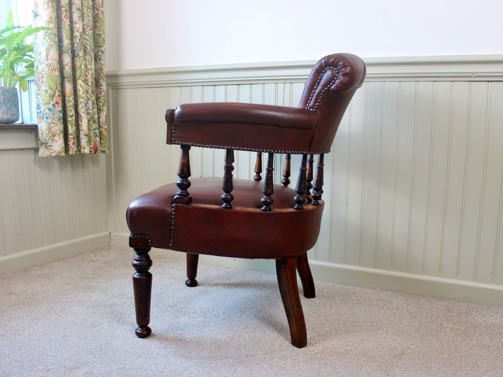 A Victorian oak elbow chair featuring deep buttoned reddish-brown leather upholstery, turned spindles, metal stud trim, and turned front legs. View VI